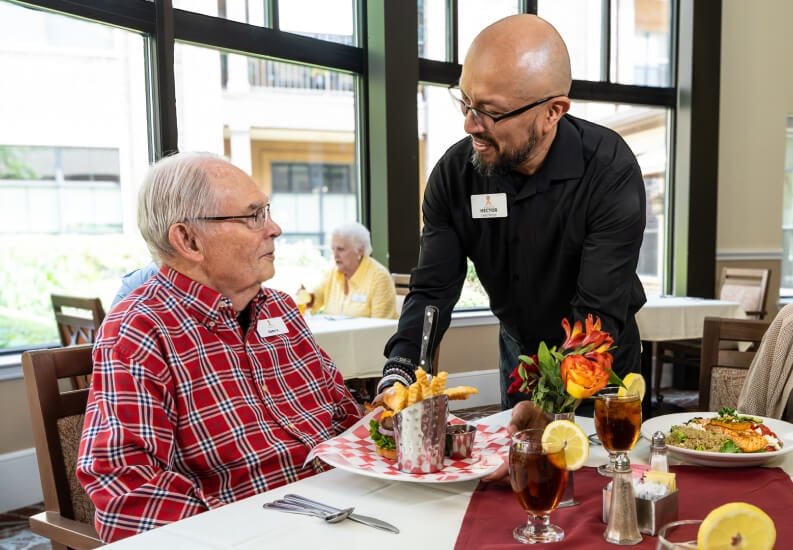 Smiling Staff Member Serves Lunch to a Senior Man in an Independent Living Facility Smiling Staff Member Serves Lunch to a Senior Man in an Independent Living Facility