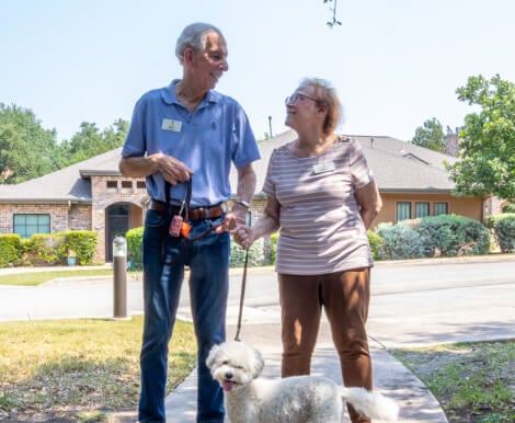 Senior Couple Walking Their Dog Outdoors of Independent Living Facility Senior Couple Walking Their Dog Outdoors of Independent Living Facility